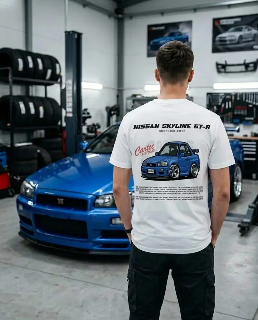 Mężczyzna w białej koszulce z rysunkowym nadrukiem Nissana Skyline GT-R R34 na tle niebieskiego auta